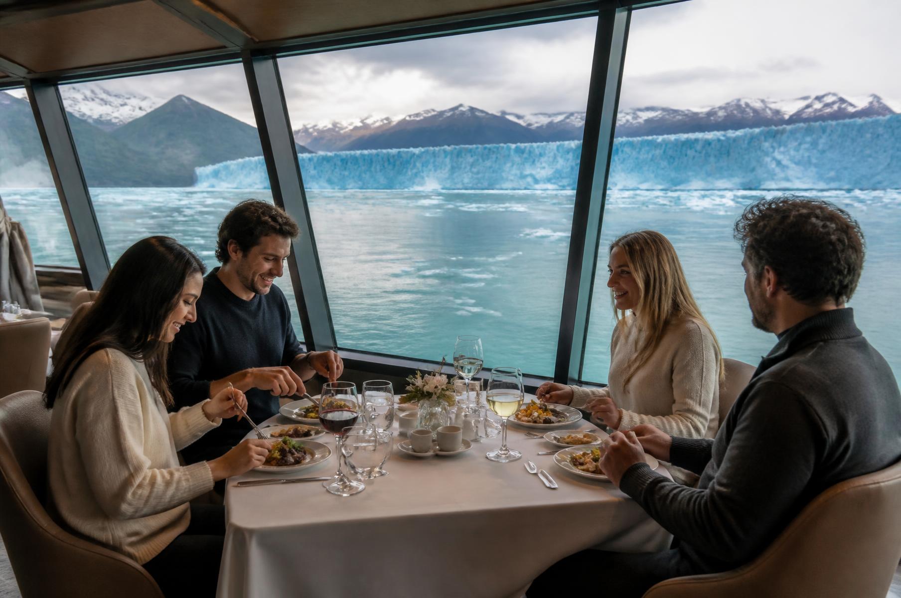 Almuerzo privado para cuatro viajeros en un salón panorámico navegando frente a los hielos patagónicos, con platos argentinos y vino servido en copas